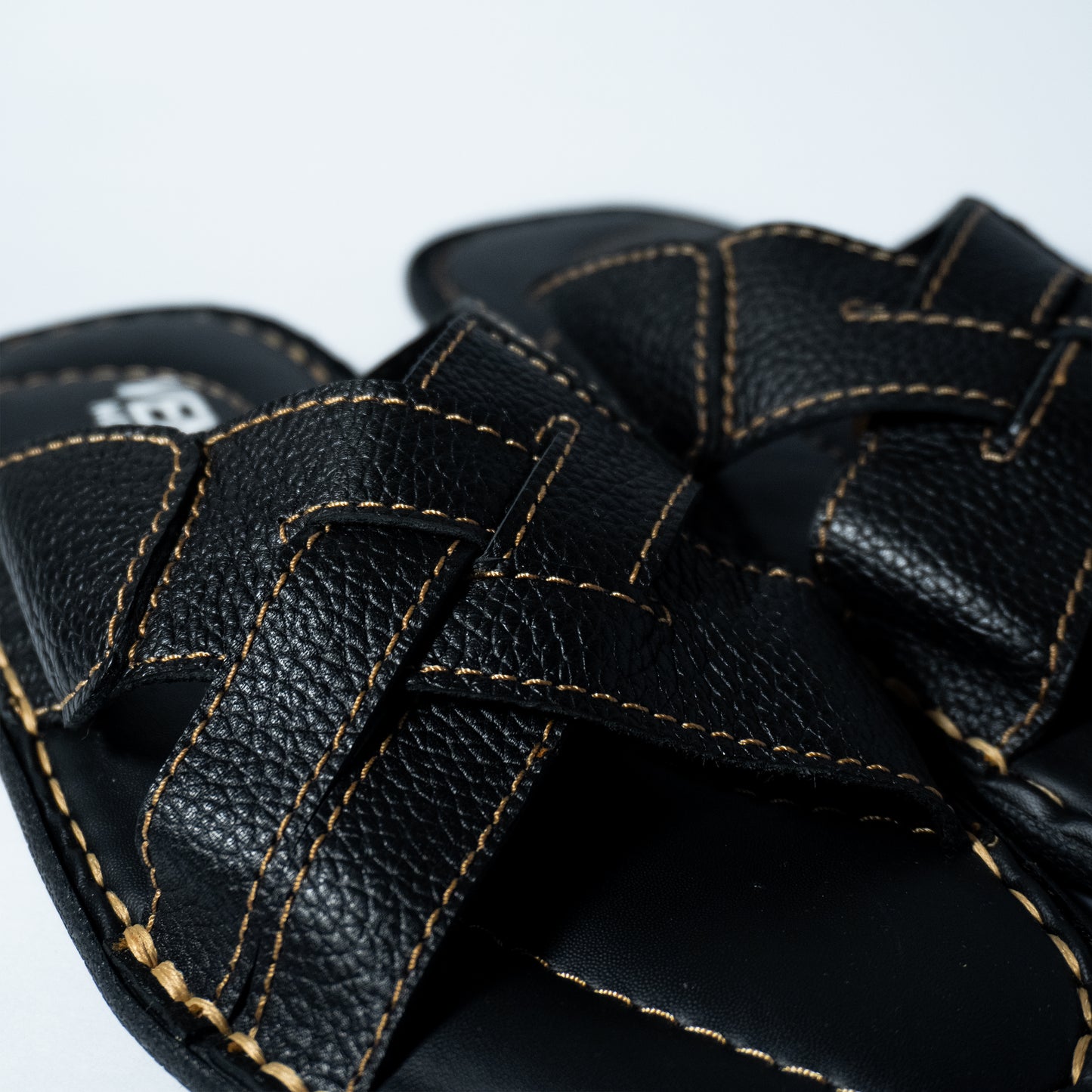 Close-up of black leather sandals with visible stitching on a light gray background