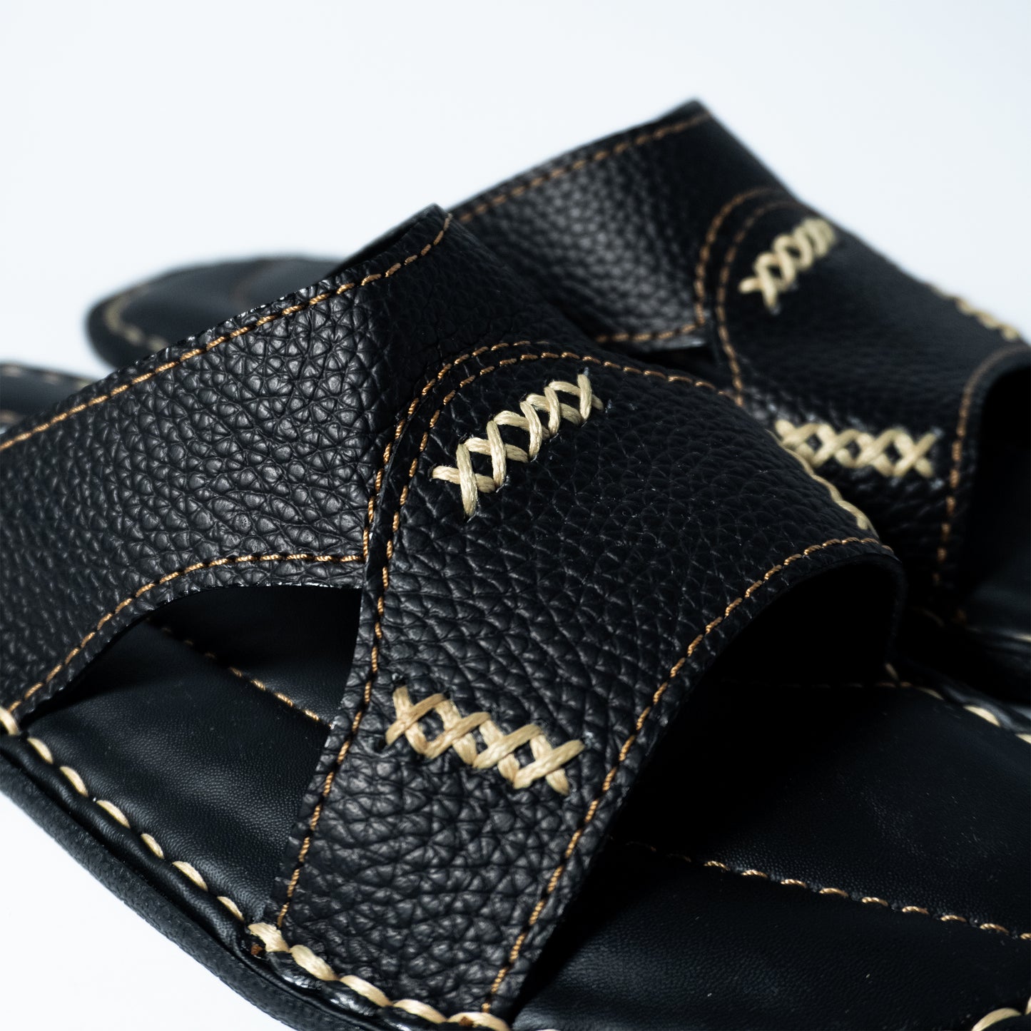 Close-up of a black leather sandal with stitching design on a white background