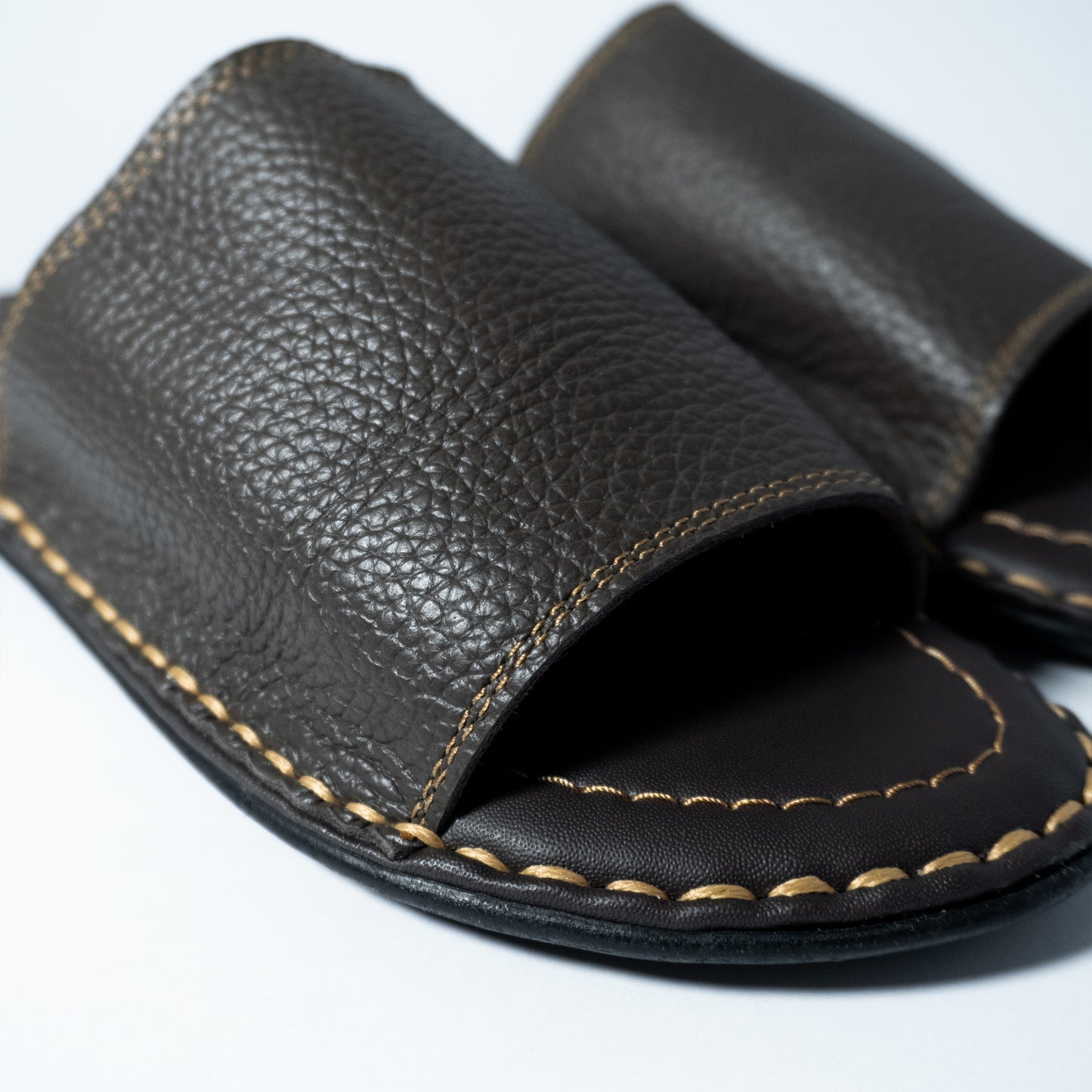 Close-up of a brown leather sandal with visible stitching on a white background