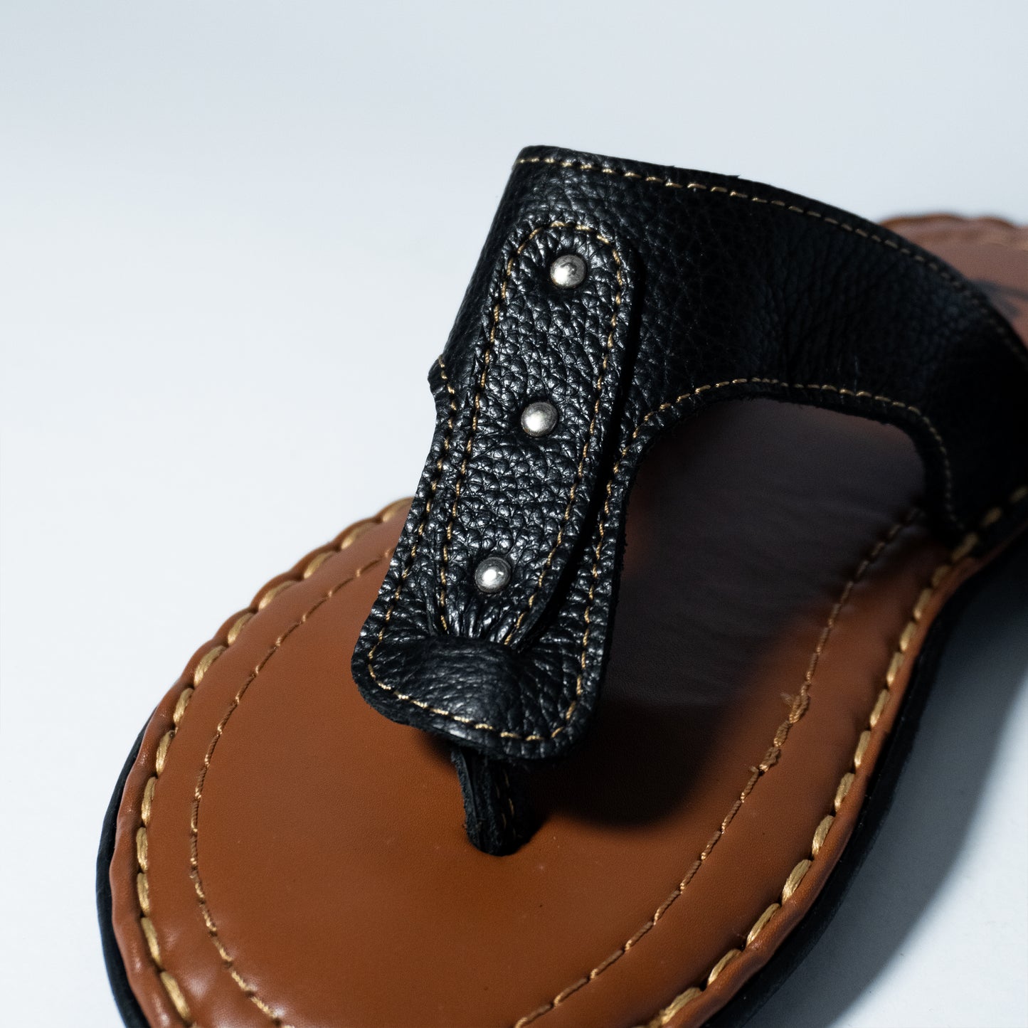 Close-up of a sandal with black strap and brown sole on a light gray background