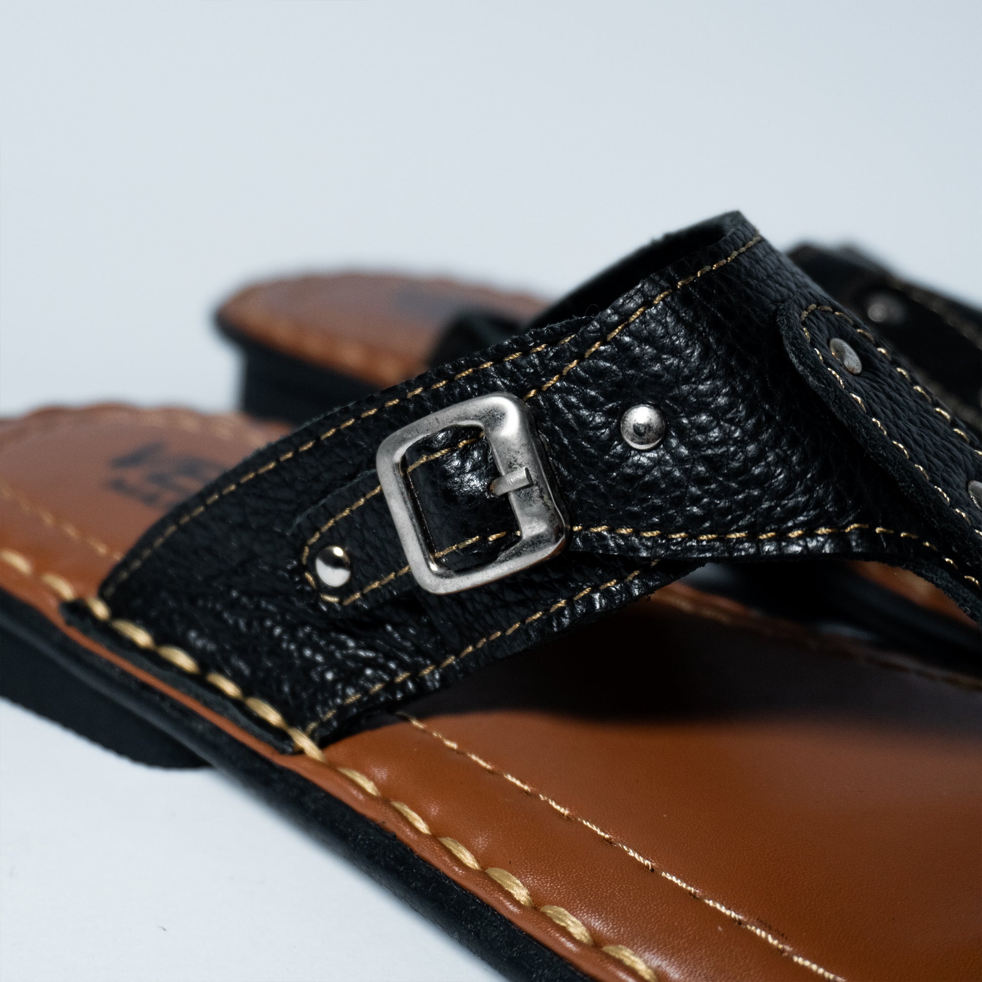 Close-up of a sandal with a black strap and silver buckle on a light gray background