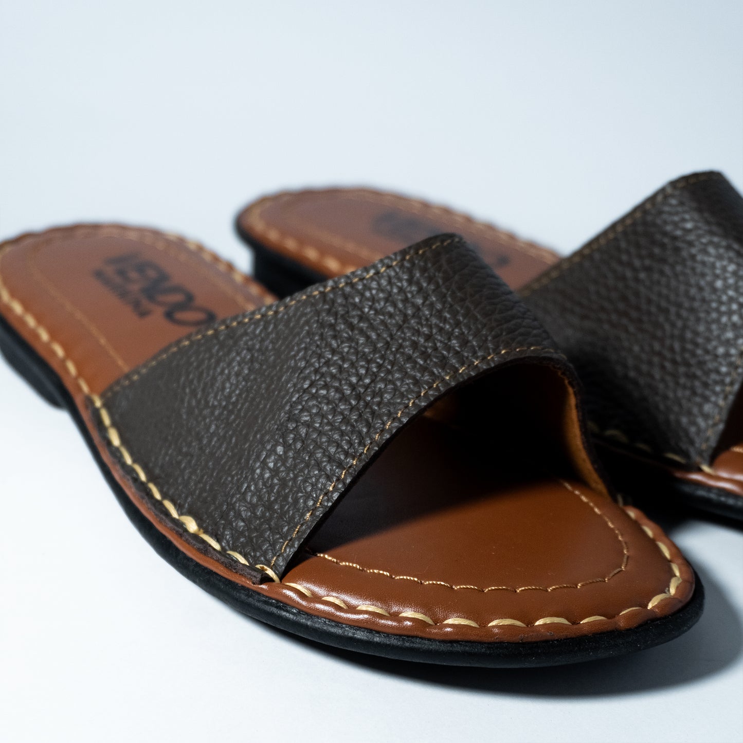 Brown leather sandal with brand name on a light gray background