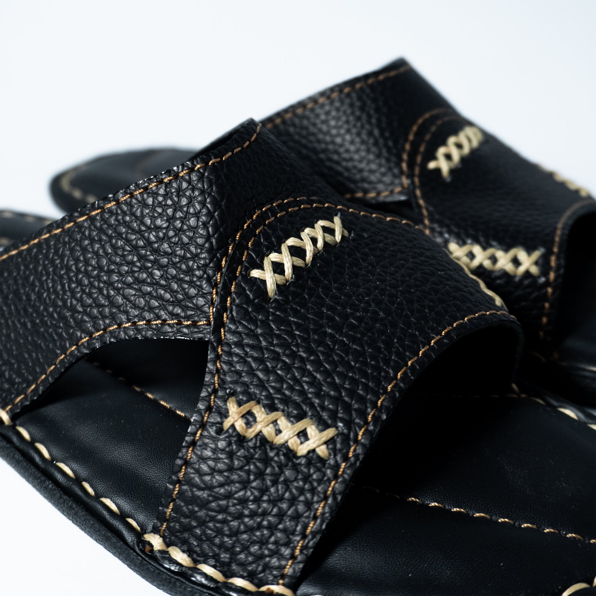 Close-up of a black leather sandal with stitching design on a white background