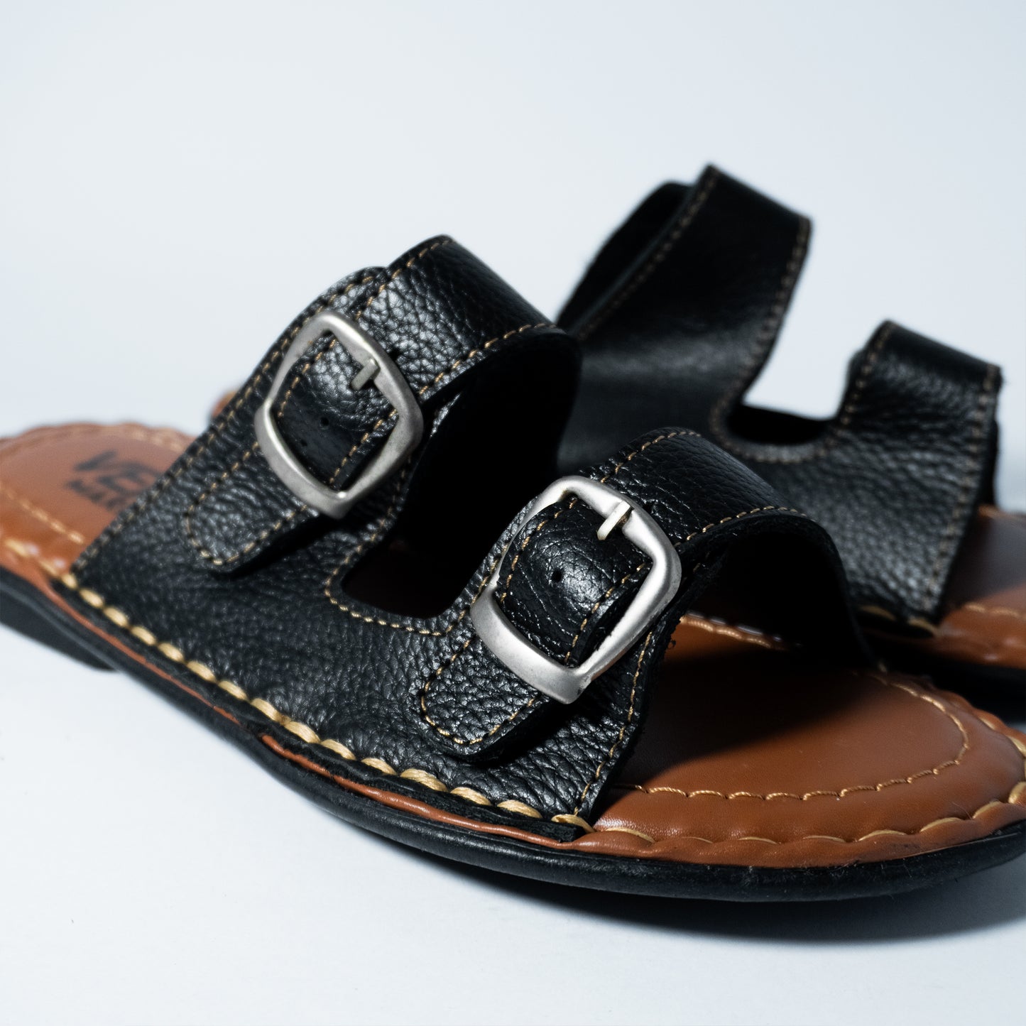 Black leather sandal with silver buckles on a light gray background